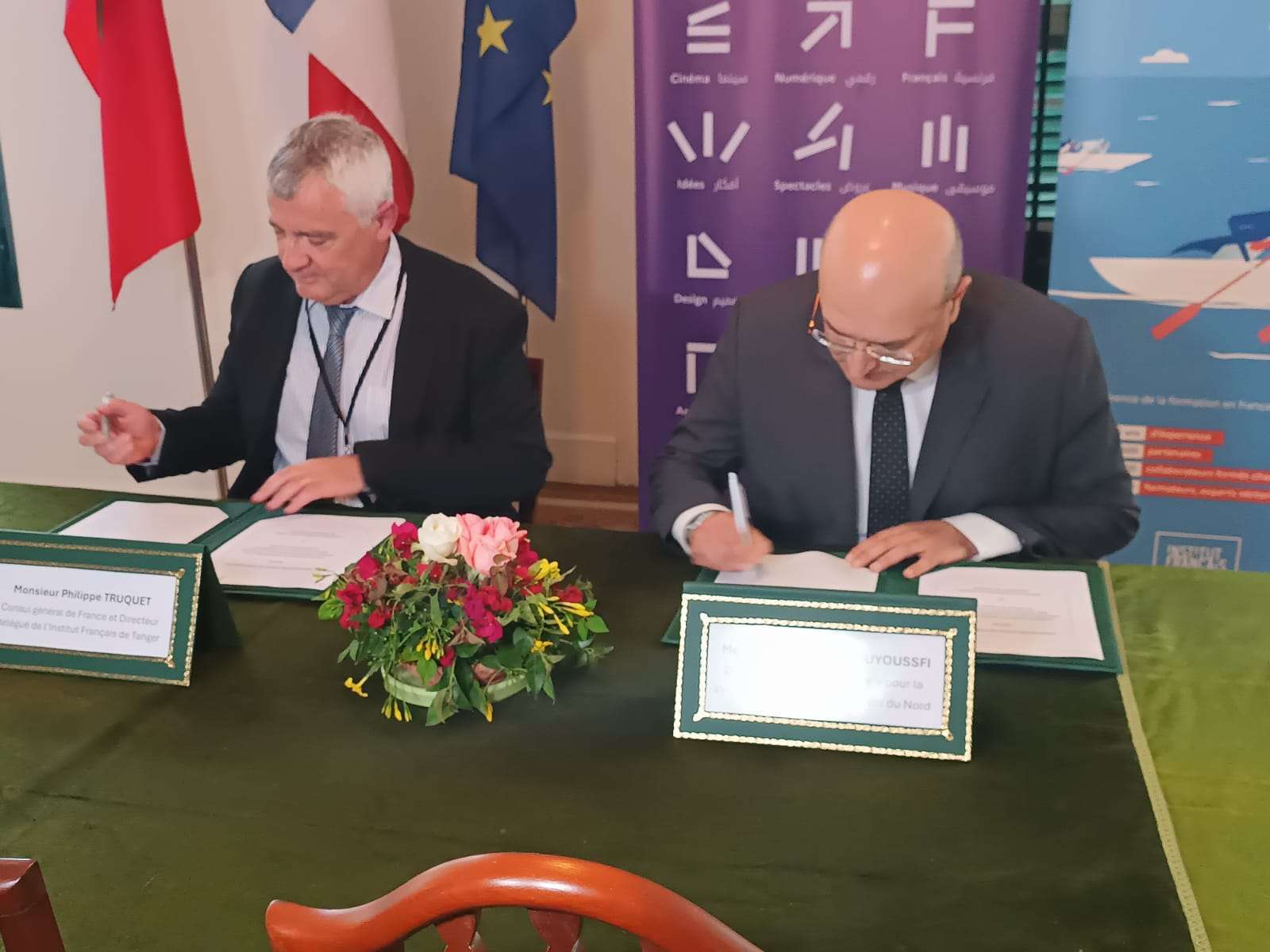 two men sitting at a table with a sign on it