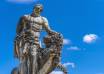 Statue représentant Hercule, héros mythologique grec, maîtrisant un lion, sous un ciel bleu avec quelques nuages.